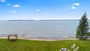 A grassy area with a swing set, a small fire pit with chairs, and a view of a calm body of water. - Million Dollar View | Lakefront Studio Cottage w/ Mackinac Bridge & Island Views (Cheboygan)