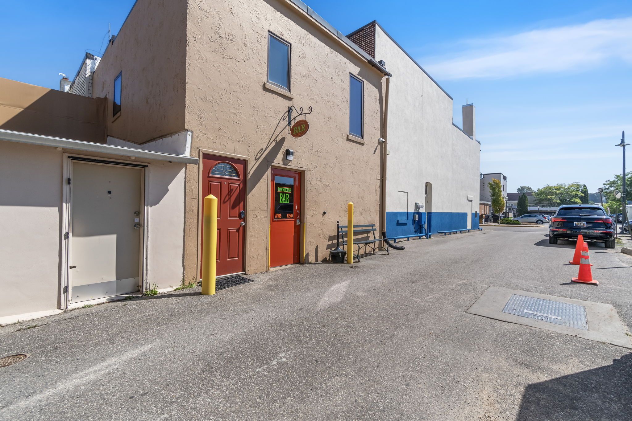 A building with a red door, a yellow bollard, and a blue bench.