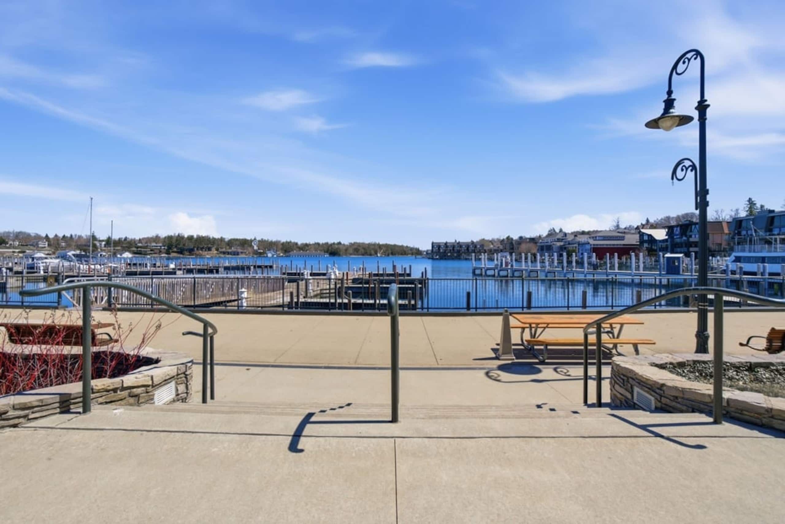 A waterfront promenade with a bench, a lamp post, and a view of the marina.