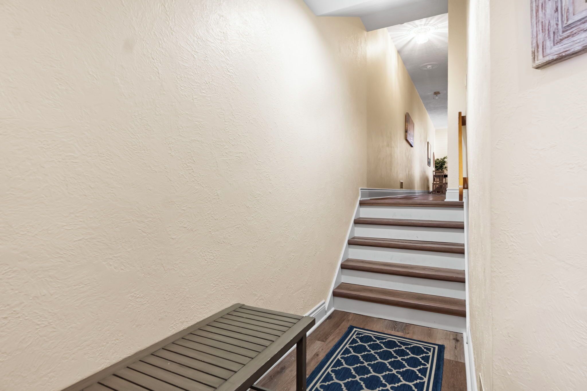 A hallway with a wooden bench, a patterned rug, and a staircase with wooden steps.