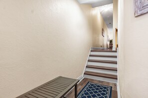 A hallway with a wooden bench, a patterned rug, and a staircase with wooden steps. - Downtown Charlevoix Balcony Loft | Walk to Bridge St, Dining & Marina (Charlevoix)