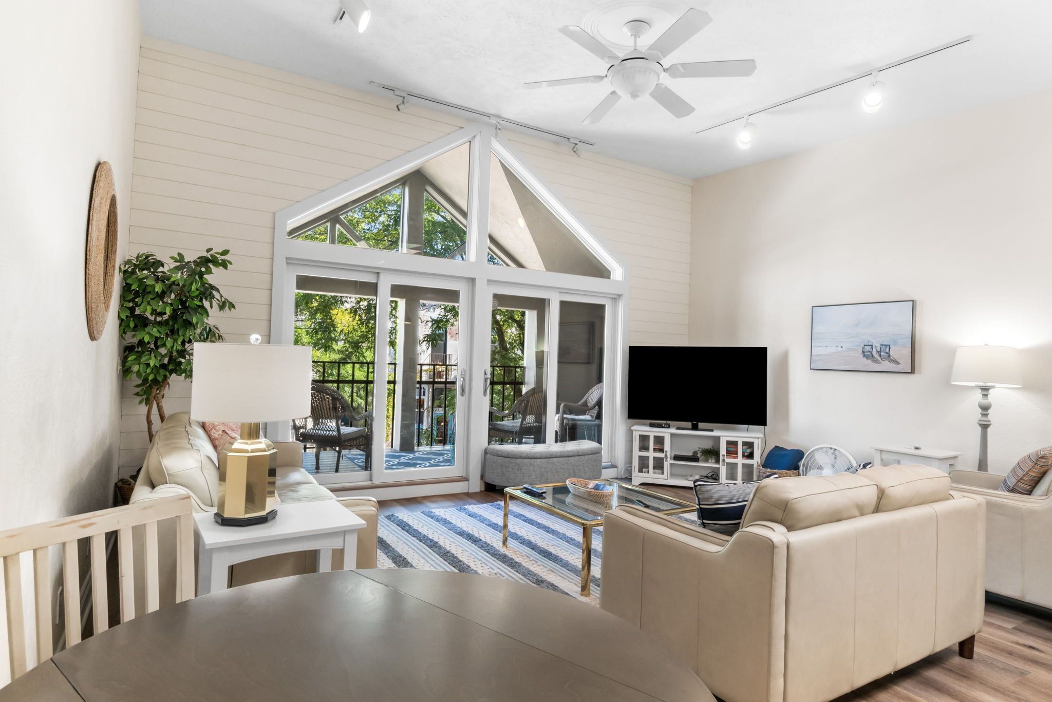 A spacious living room with a high ceiling, a television, a sofa, a dining table, and a large window.