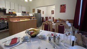 A dining area with a buffet setup, including a fruit bowl, dining tables, chairs, and a refrigerator in the background.