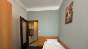 A hotel room with a single bed, a small wooden nightstand, a door leading to a bathroom, and a light blue wall with a framed picture.