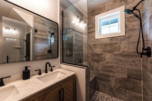 Ein Badezimmer mit Marmorwaschbecken, Holzsärchen, einem großen Spiegel und einer Dusche mit Glastür.