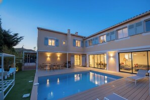 Ein zweistöckiges Haus mit Swimmingpool, Außenmöbeln und einer überdachten Terrasse.
