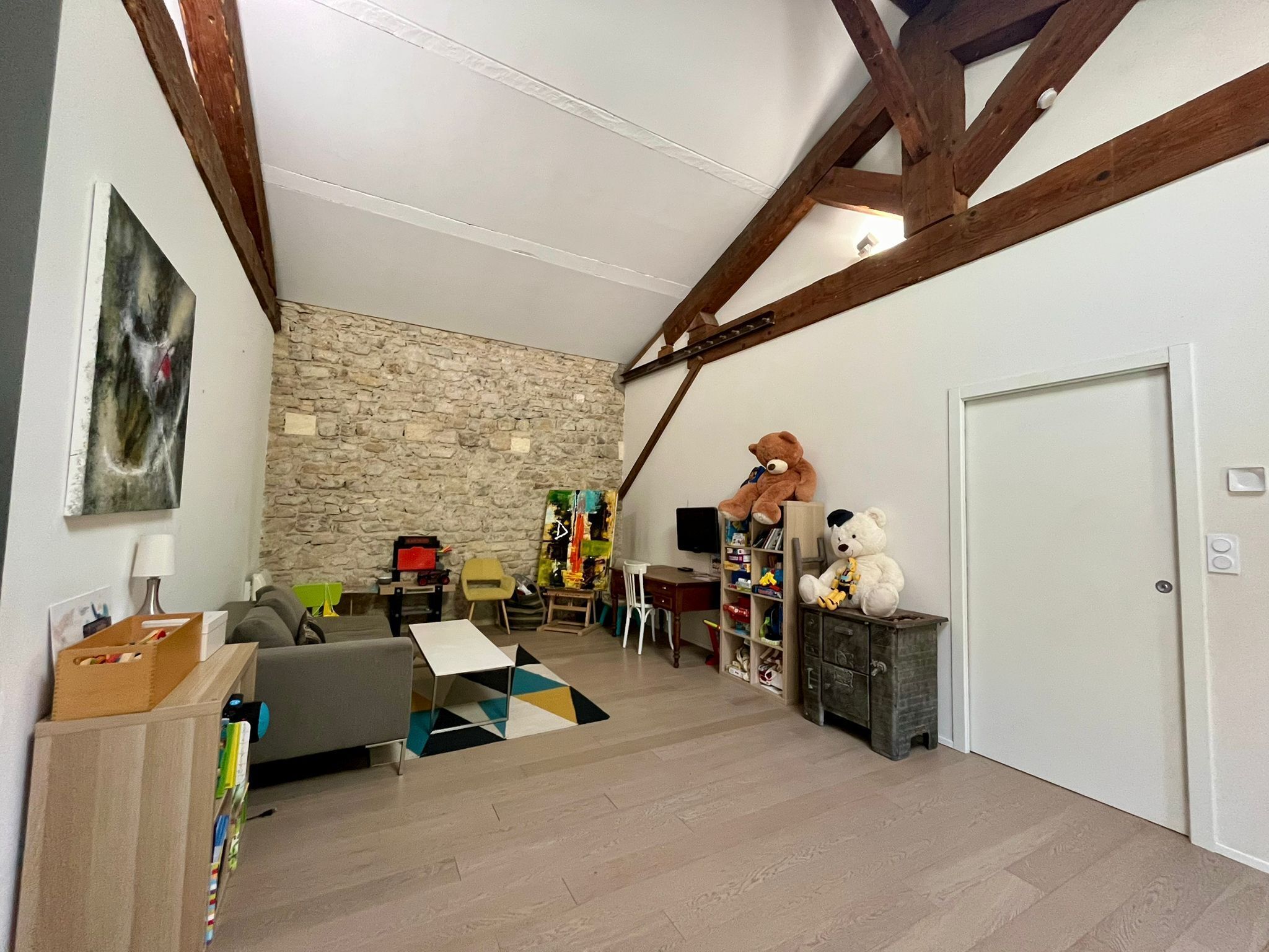 Amplia sala de estar con pared de piedra, vigas de madera, un sofá, una mesa de centro, un televisor y dos osos de peluche.