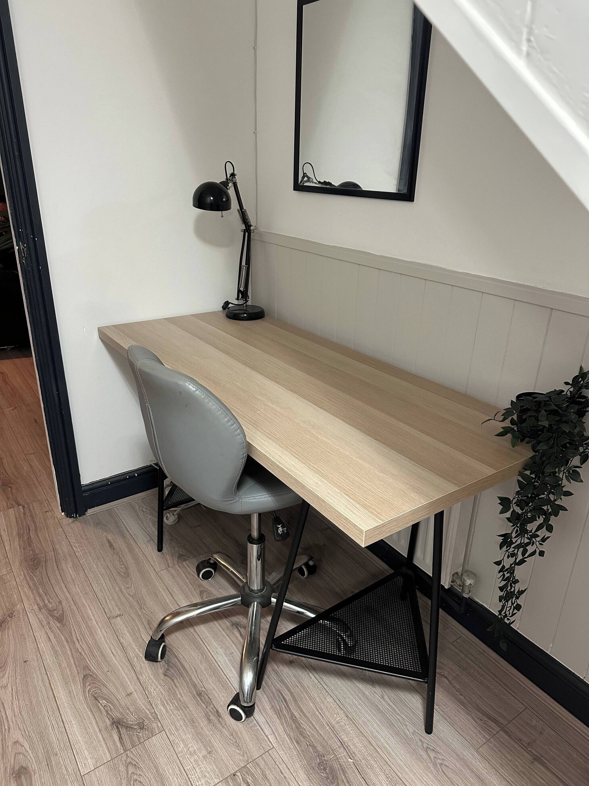 A workspace with a wooden desk, a grey office chair, a black desk lamp, and a mirror on the wall.
