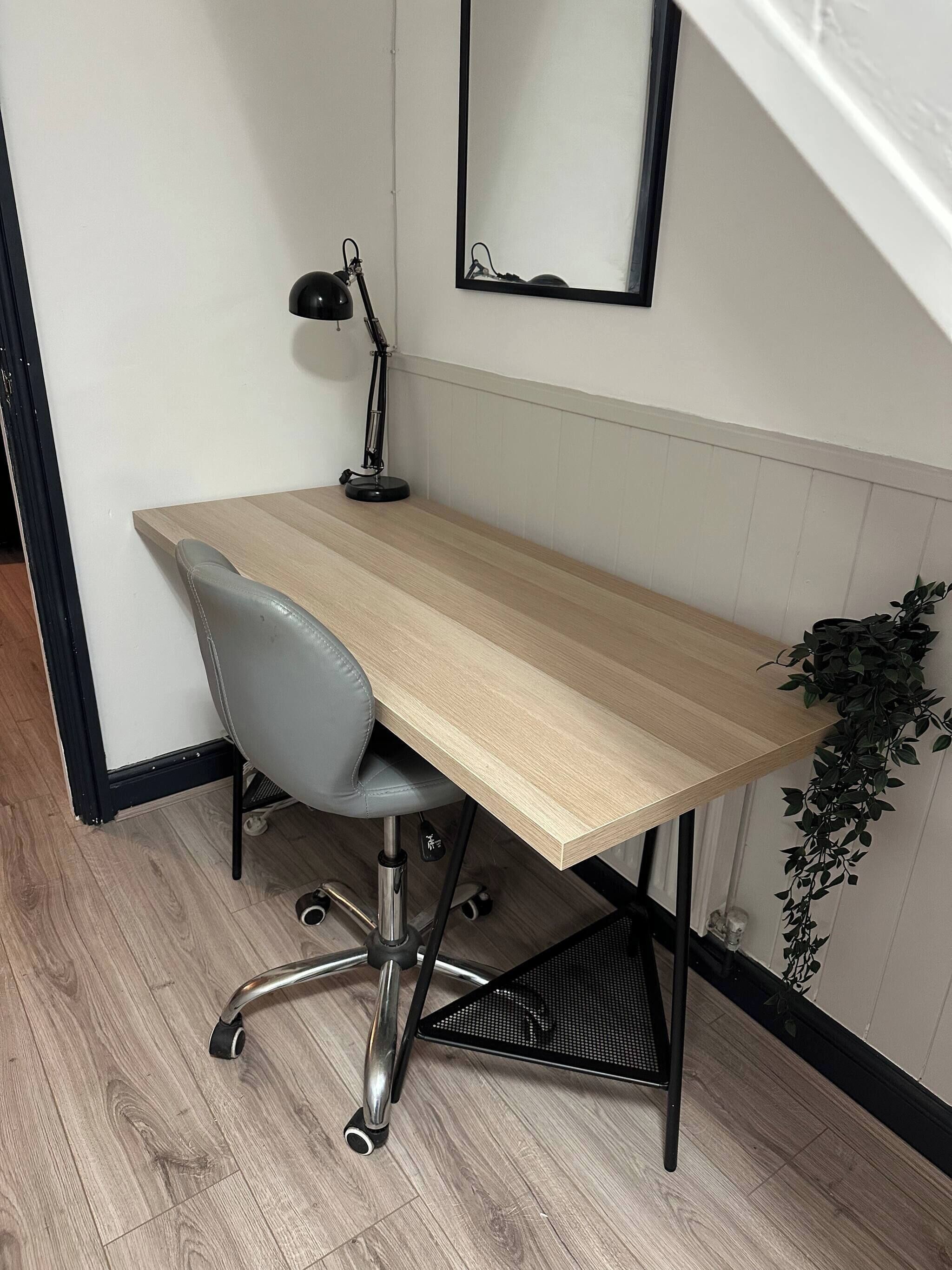 A workspace with a wooden desk, a grey office chair, a black desk lamp, and a potted plant.