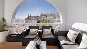 A balcony with wicker furniture, a white railing, and a view of buildings. - Spacious apartment in the heart of Albufeira (Albufeira)