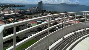 Un balcon offrant une vue sur un paysage urbain côtier, avec des bâtiments et une étendue d’eau.