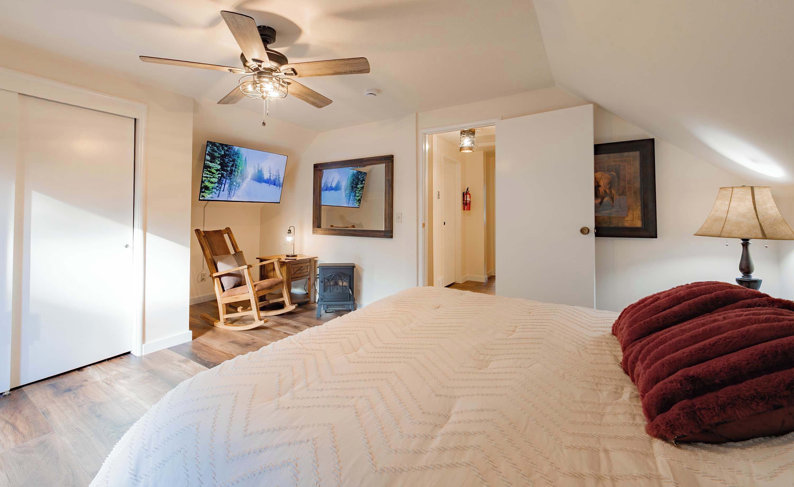 Une chambre à coucher avec un grand lit, un fauteuil à bascule, un ventilateur de plafond, une télévision et une cheminée.