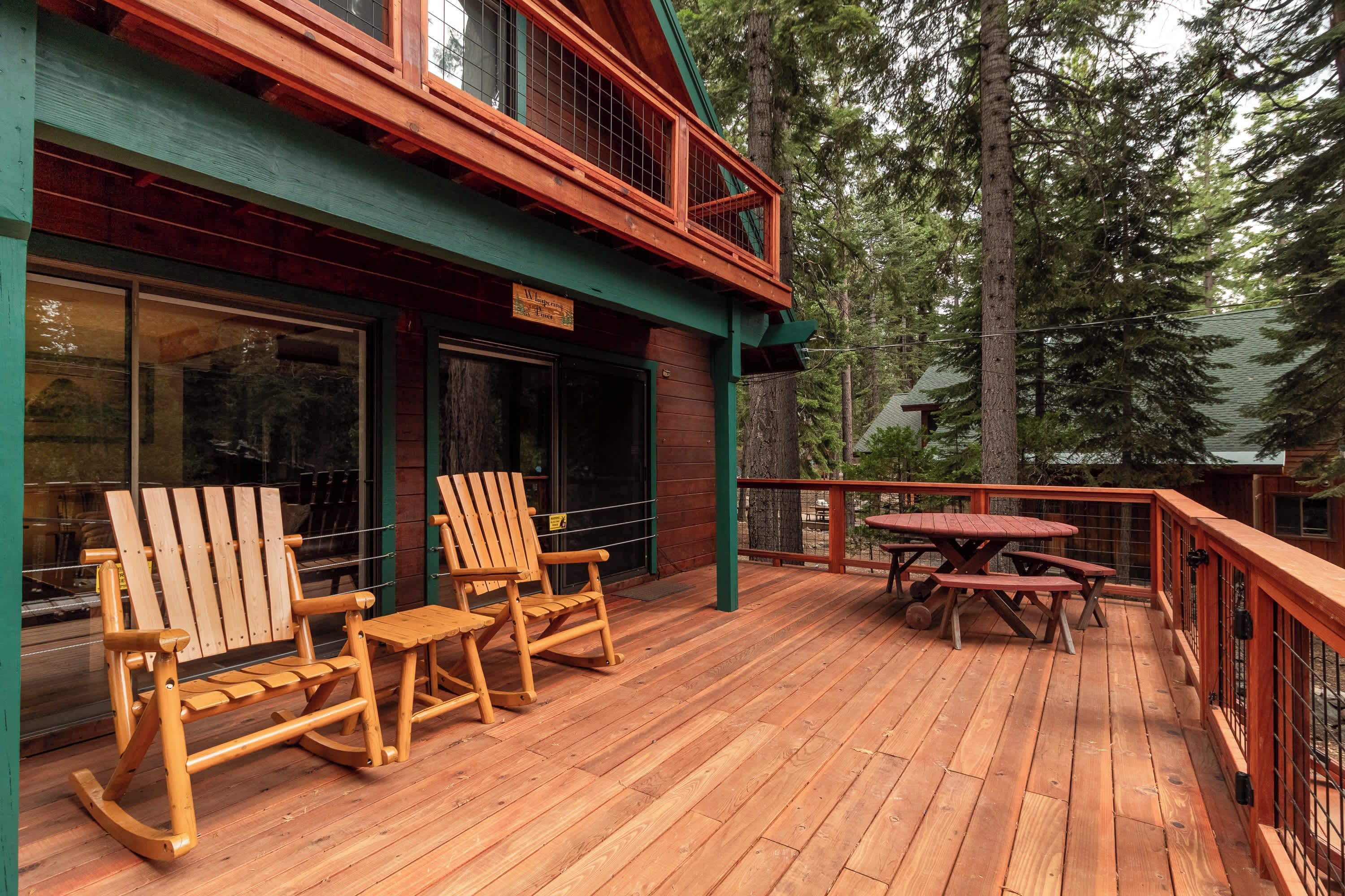 A wooden deck with two rocking chairs and a picnic table, surrounded by a forest.