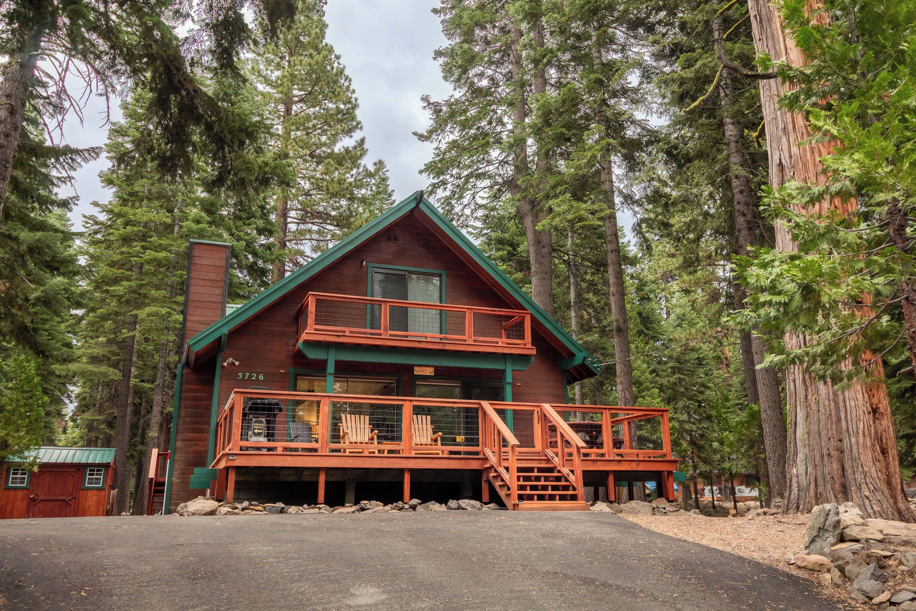 A two-story cabin with a balcony, surrounded by tall trees.