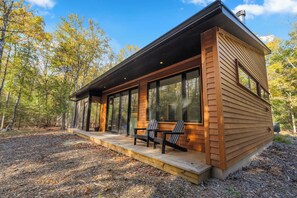 A modern cabin with large windows, a deck, and a forest backdrop.