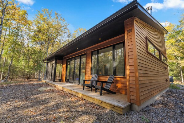 A modern cabin with large windows, a deck, and a forest backdrop.