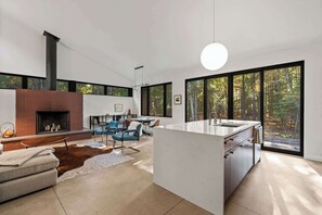 A modern interior with a fireplace, dining area, and large windows with a forest view.