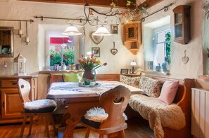 A cozy, rustic interior with a wooden dining table, chairs, a sofa, and a chandelier.