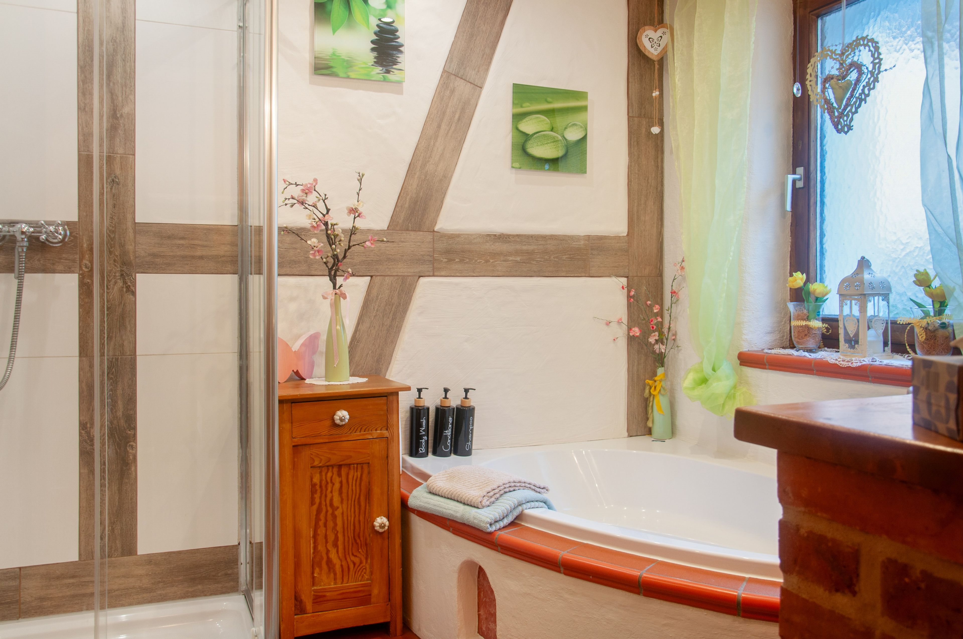 A bathroom with a wooden-framed shower, a bathtub with a towel, and a vanity with toiletries.