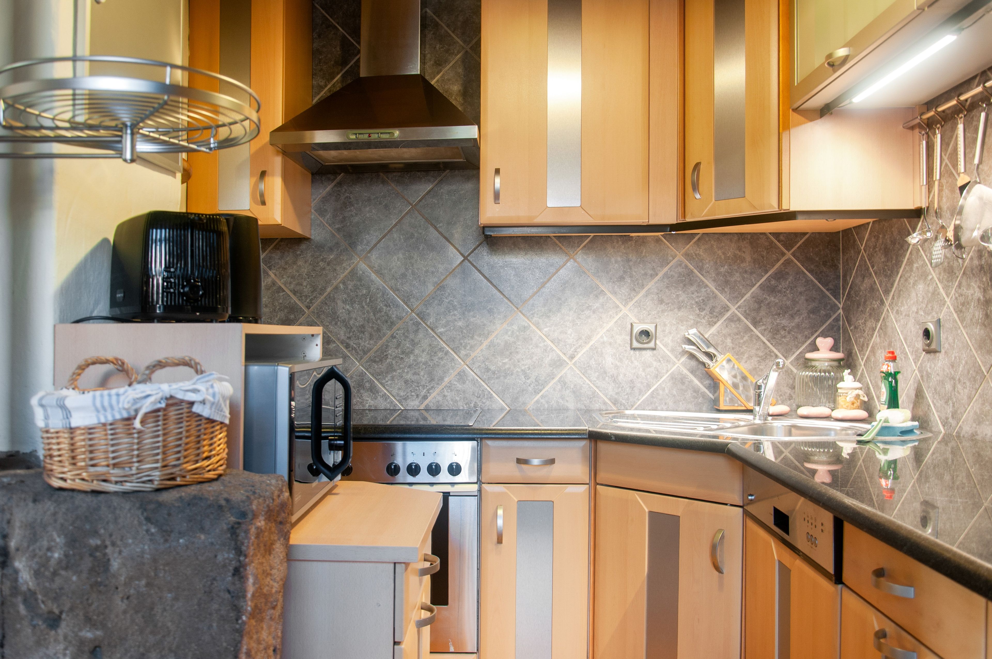 A modern kitchen with wooden cabinets, a stainless steel range hood, and a tiled backsplash.