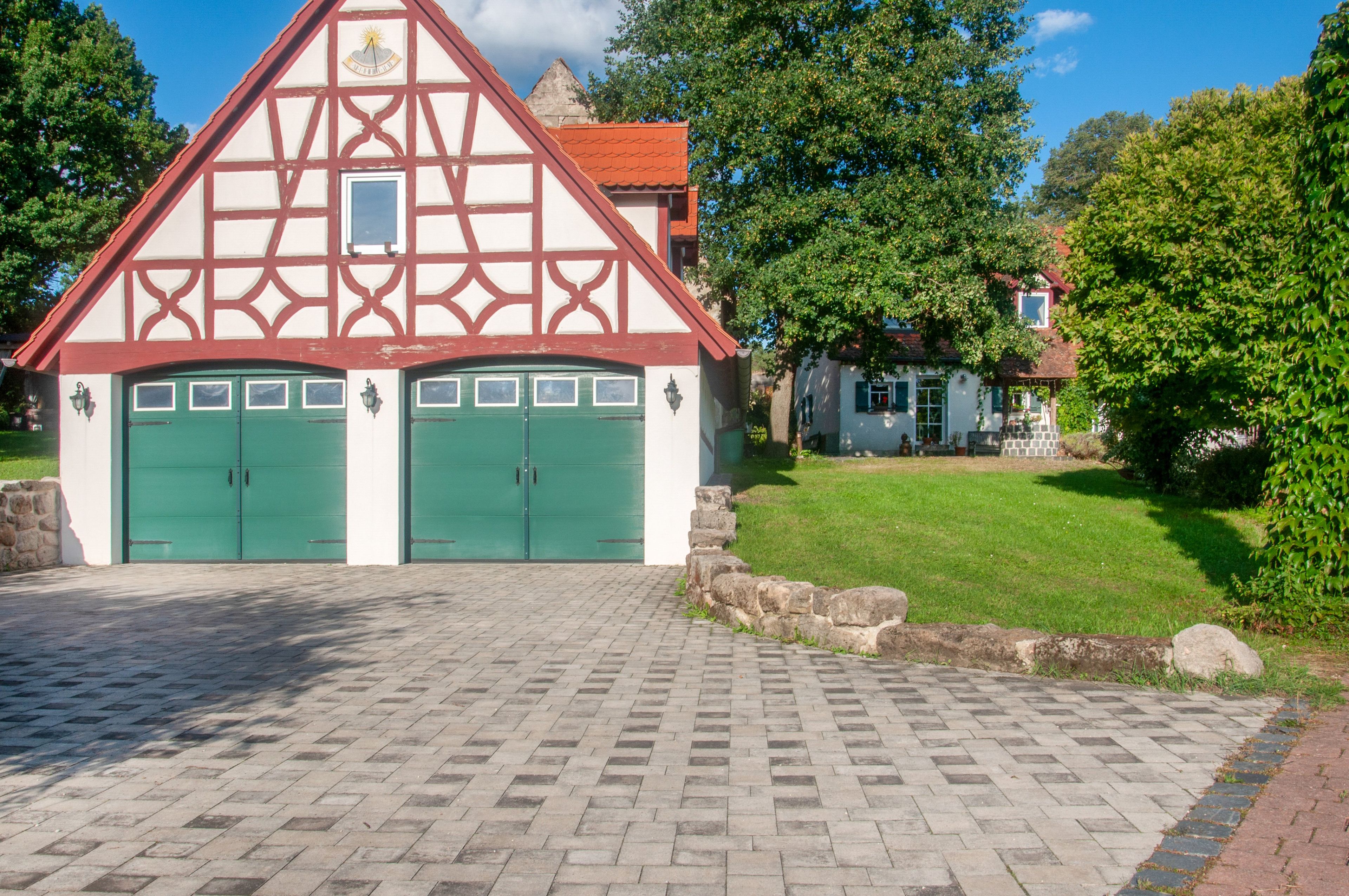 Ein traditionelles Fachwerkhäuschen mit zwei grünen Türen und einer Mauer aus Stein davor.
