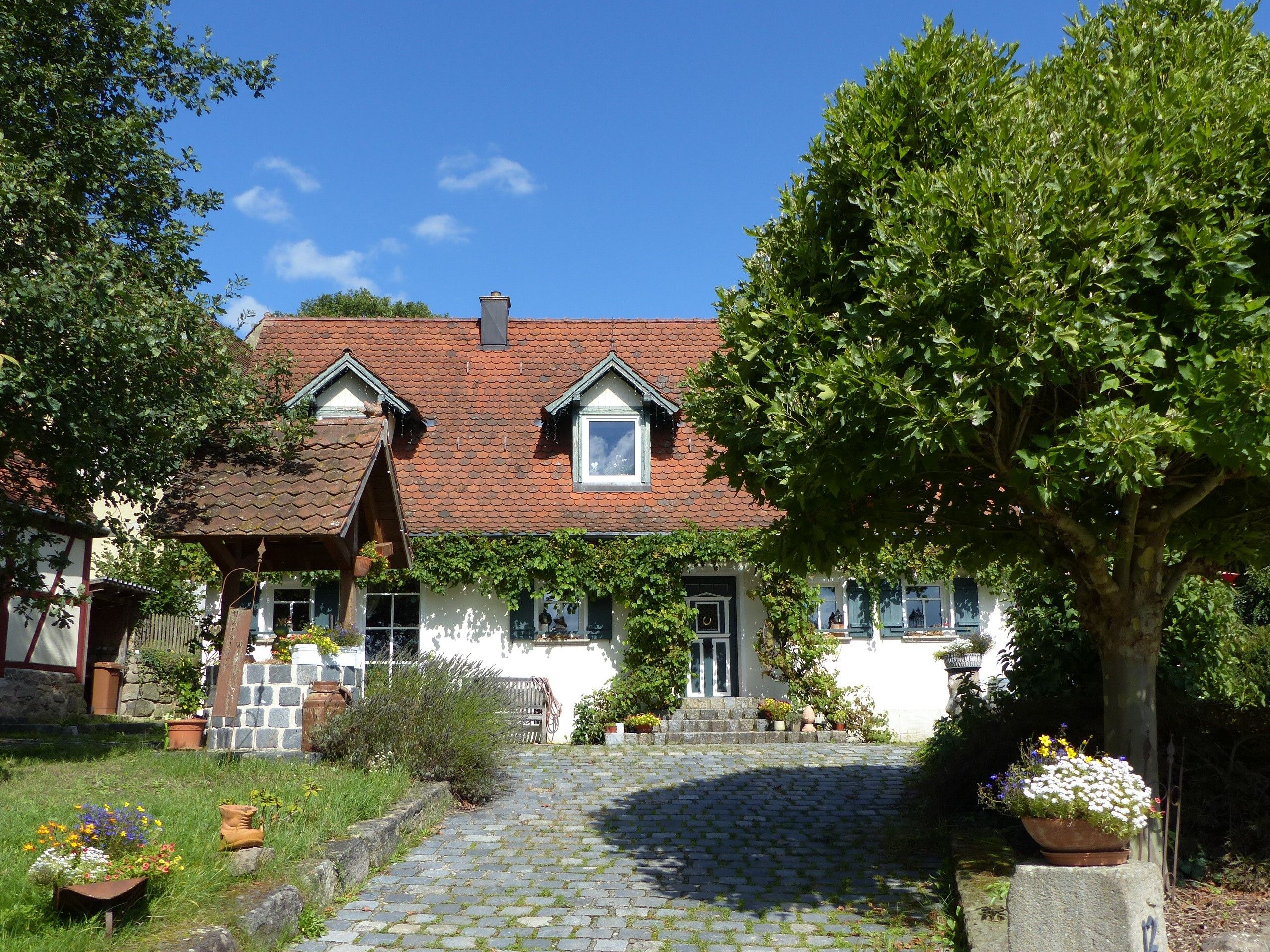 Ein traditionelles Haus mit einem Ziegeldach, einer Steintreppe, die zum Eingang führt, und einem Garten mit Blumentöpfen.