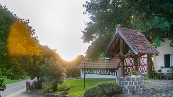 En traditionell byggnad i trä med ett tak täckt av takpannor, omgiven av en välskött trädgård med en stenlagd gångväg.
