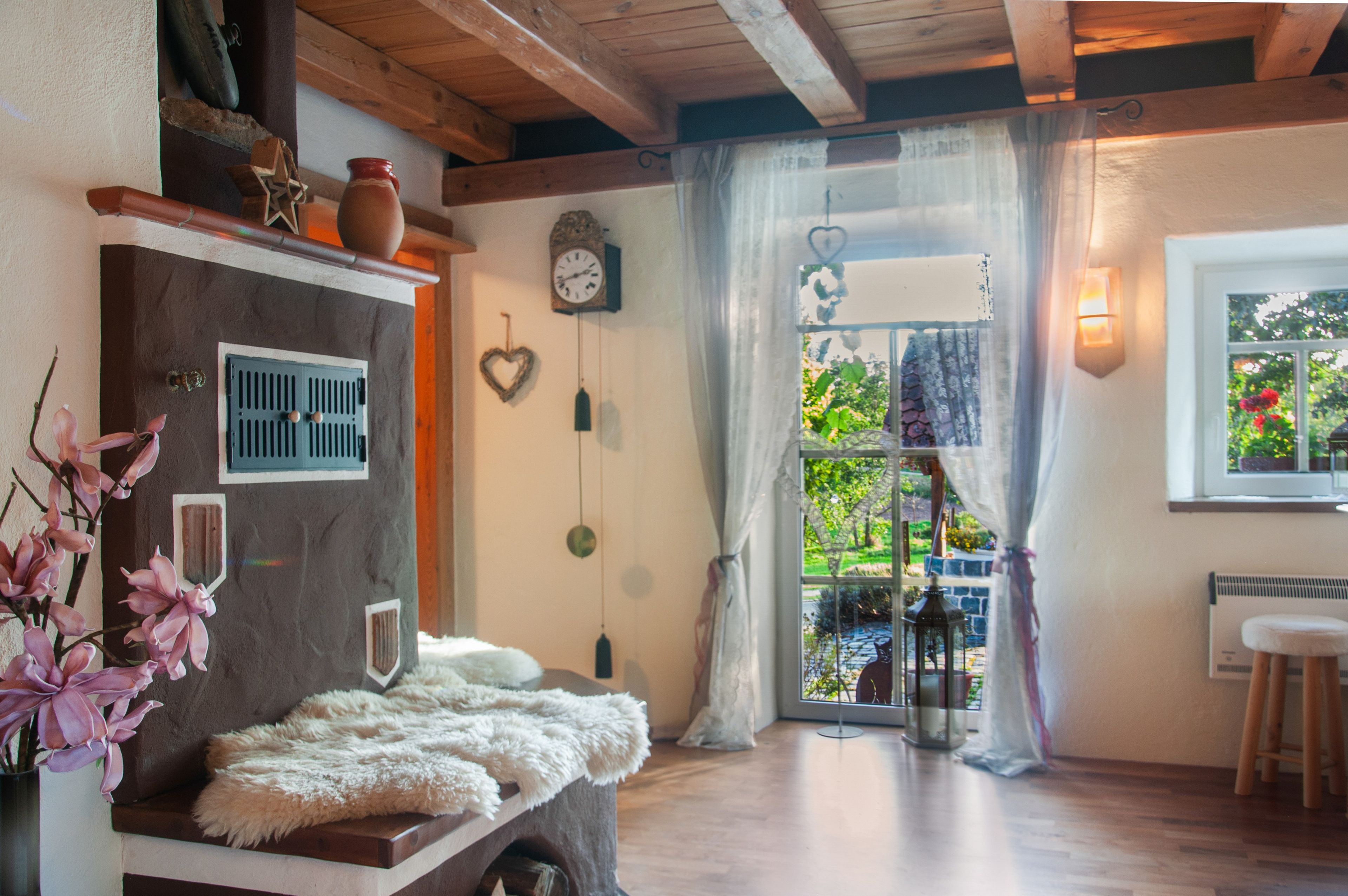 Una habitación acogedora con techo de madera, un reloj de pared rústico, un adorno con forma de corazón y vistas a un jardín a través de una ventana.