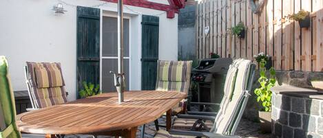 Eine Terrasse im Freien mit einem Holztisch und -stühlen, einem Grill und einem roten Sonnenschirm.
