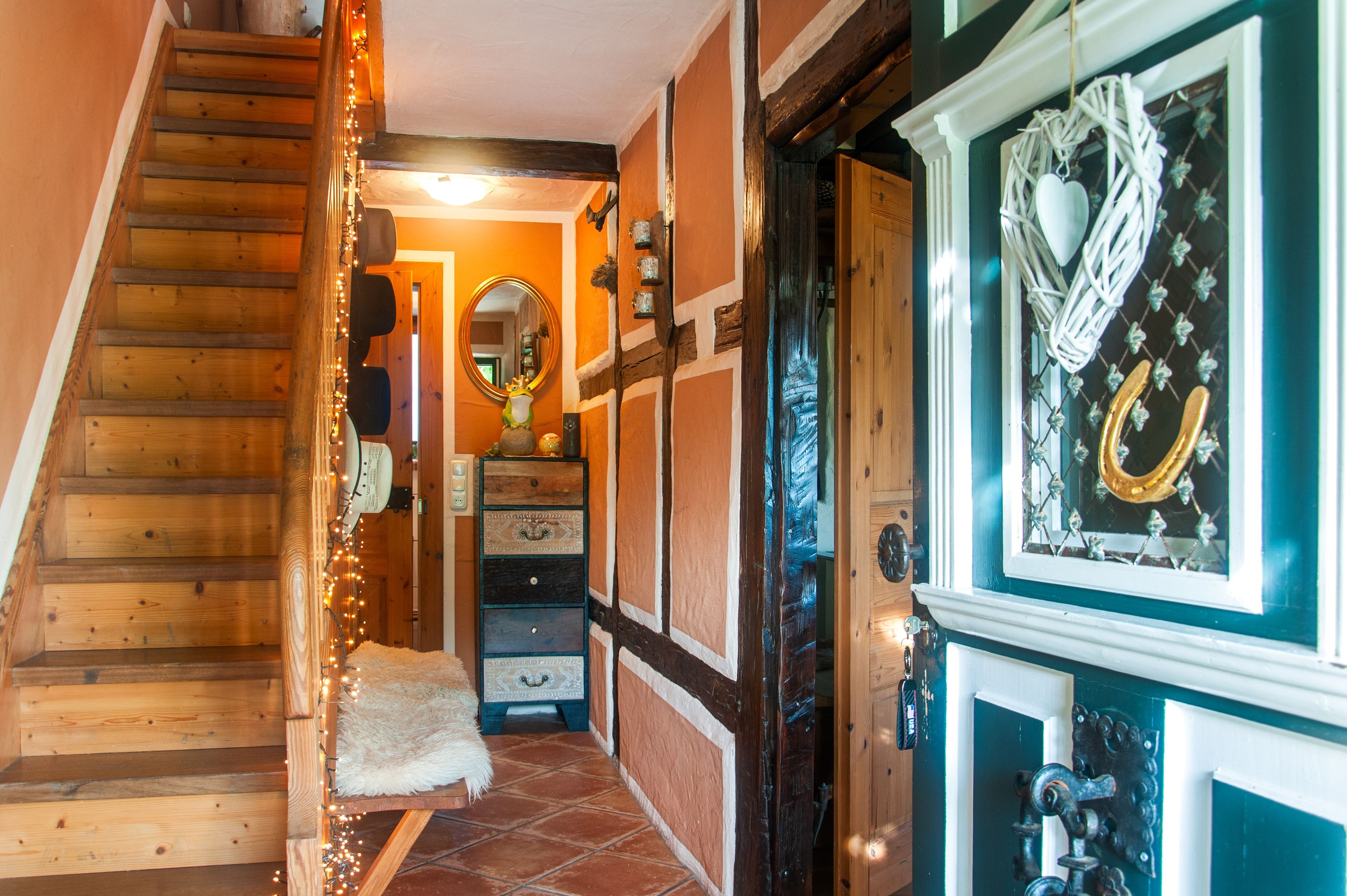Escada de madeira que leva a um quarto com um tapete branco e fofo, um espelho e uma porta com um arranjo decorativo.