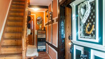 Escada de madeira que leva a um quarto com um tapete branco e fofo, um espelho e uma porta com um arranjo decorativo.