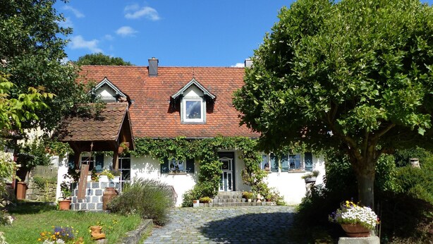 A traditional house with a tiled roof, a stone pathway leading to the entrance, and a garden with potted plants.
