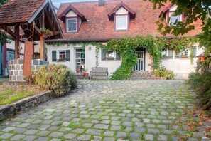 Une maison traditionnelle avec une allée pavée, une pergola en bois et un mur en pierre.