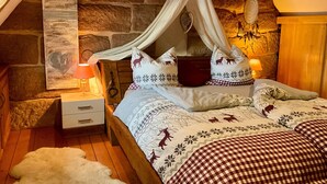 A cozy bedroom with a stone wall, a bed with a canopy, a nightstand with a lamp, and a decorative wall piece.
