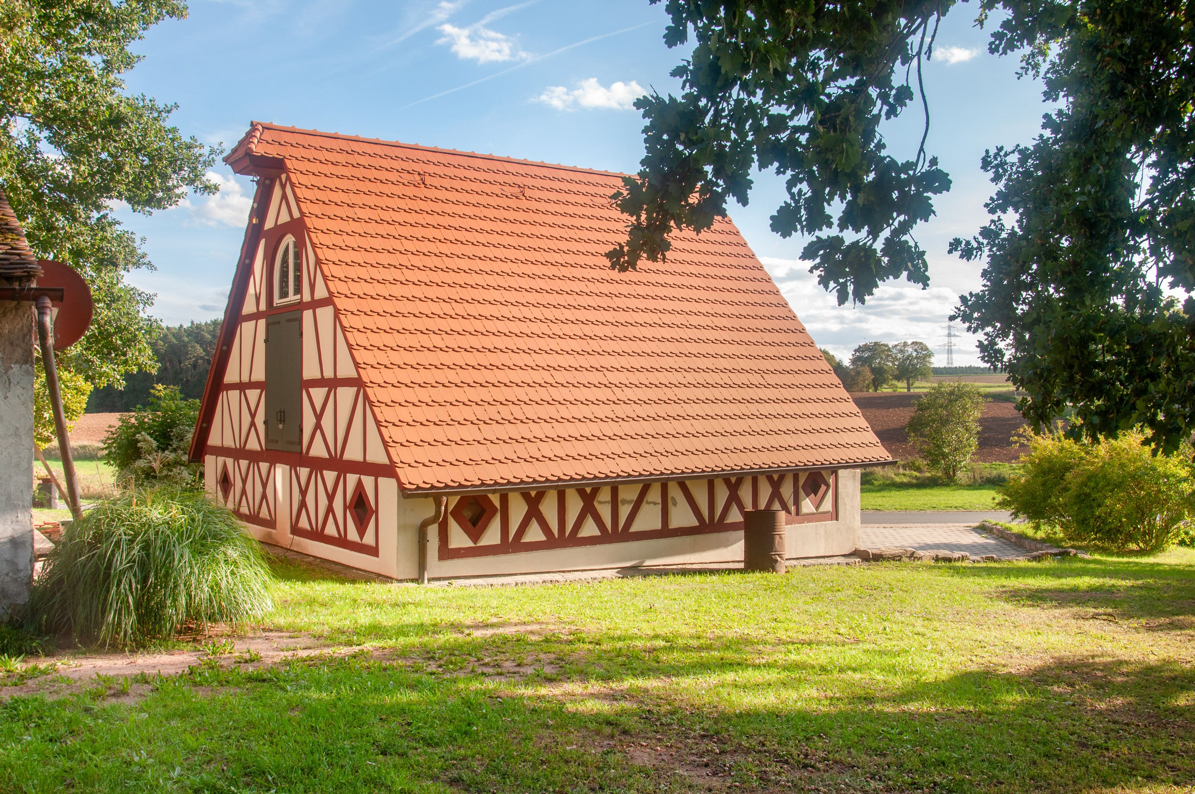 Una casa tradicional con entramado de madera y techo inclinado, rodeada de vegetación y un cielo despejado.