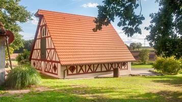 Una casa tradicional con entramado de madera y techo inclinado, rodeada de vegetación y un cielo despejado.