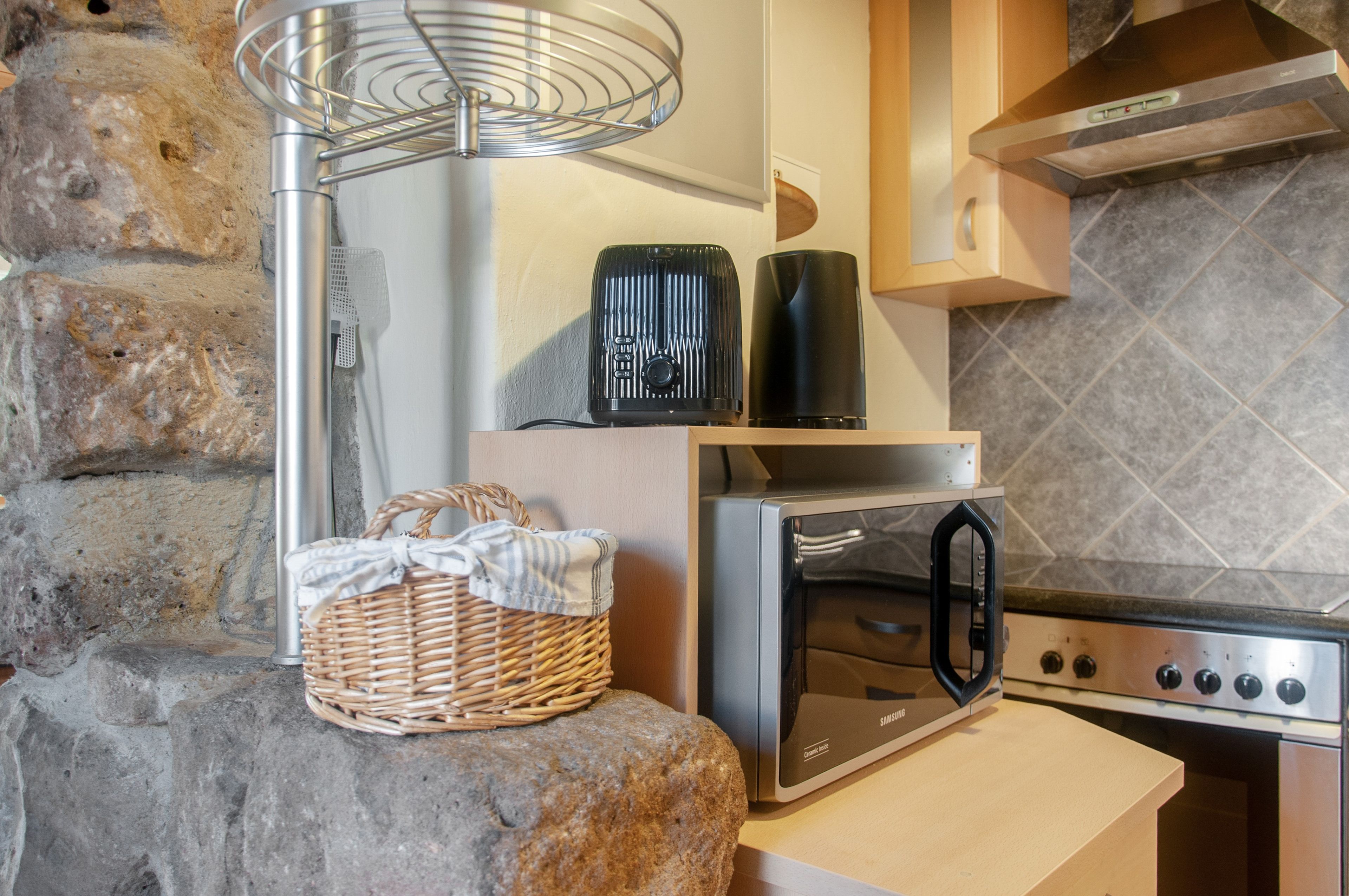 A kitchen with a stone wall, a stainless steel oven, a microwave, and a kettle on the countertop.