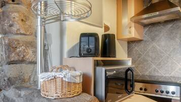 A kitchen with a stone wall, a stainless steel oven, a microwave, and a kettle on the countertop.