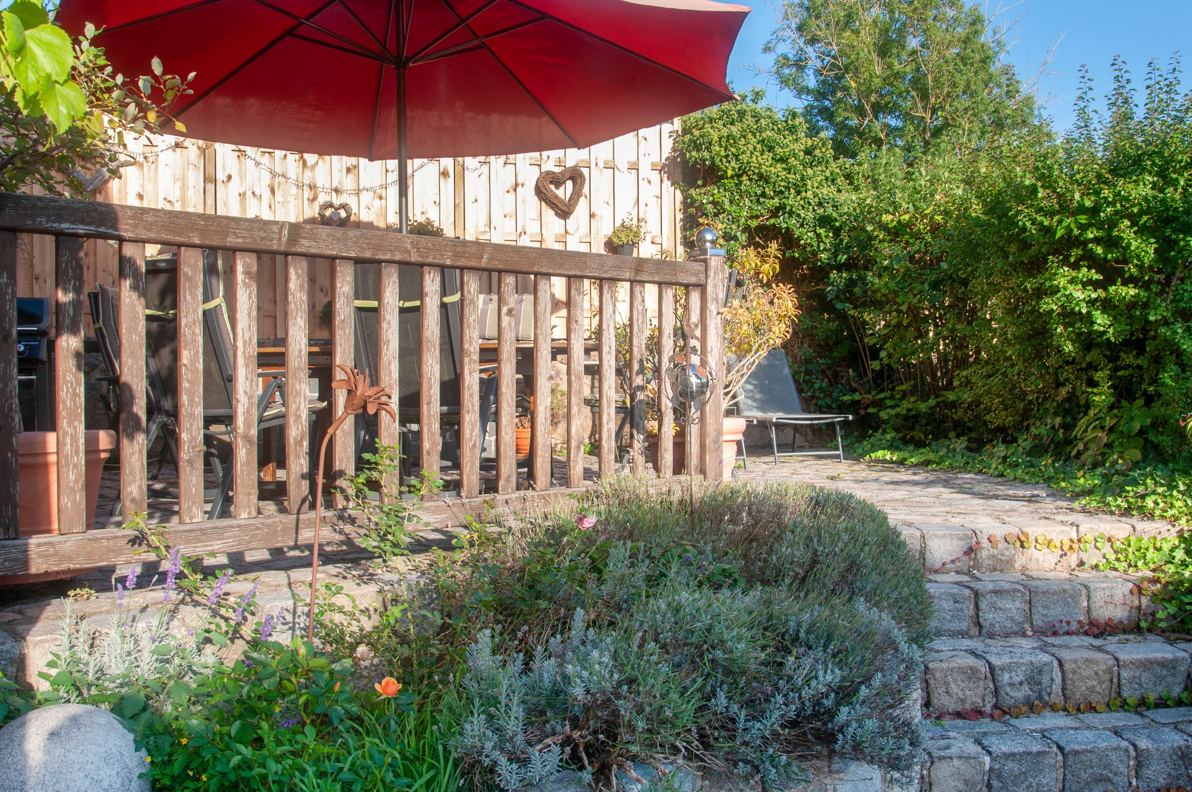 A wooden deck with a red umbrella, surrounded by greenery and stone steps.