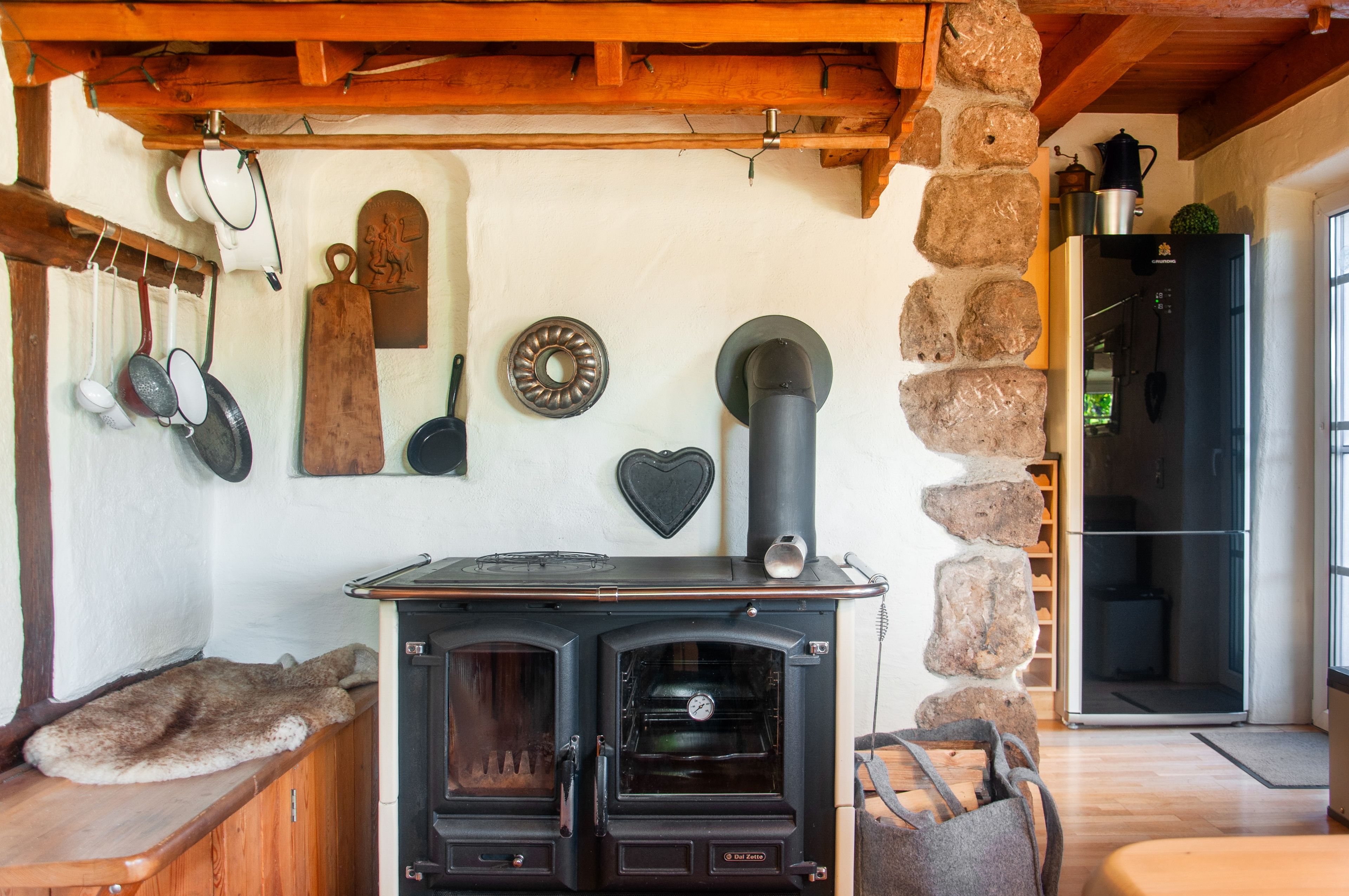 Une cuisine rustique avec un poêle à bois, un mur en pierre et divers ustensiles de cuisine accrochés au mur.