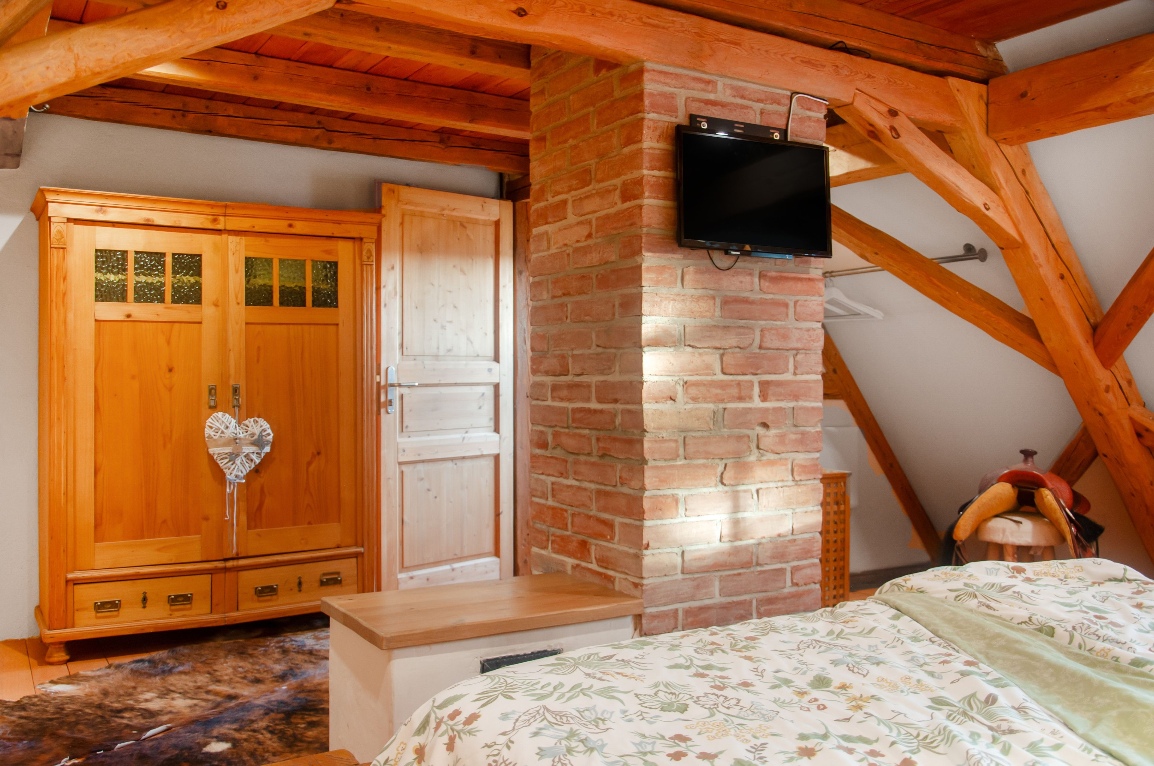 A bedroom with a wooden ceiling, a brick fireplace, a wooden wardrobe, and a television mounted on the wall.