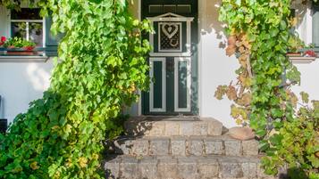 A white building with a green door, stone steps, and ivy.