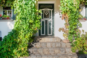 A white building with a green door, stone steps, and ivy.
