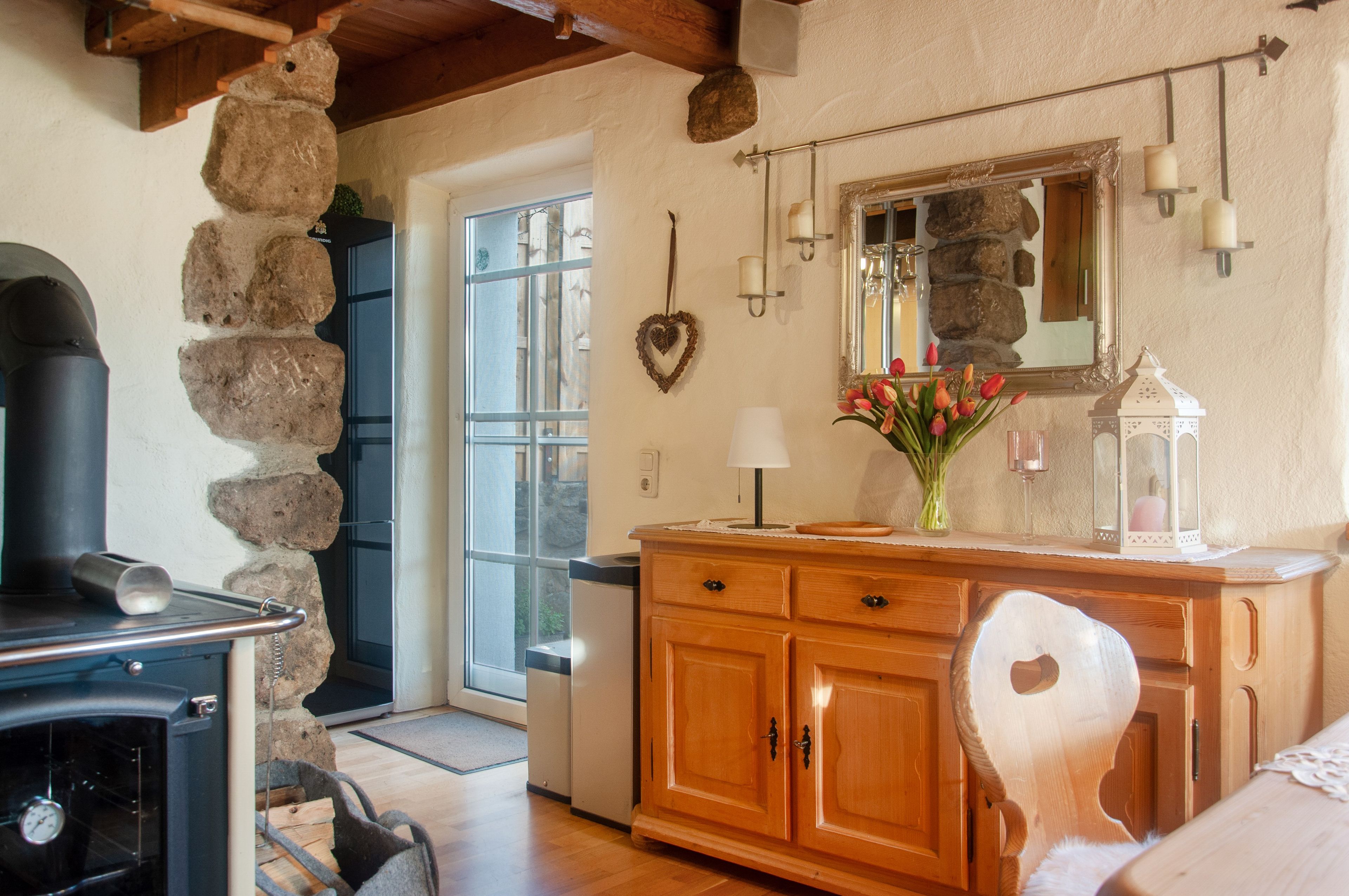 A rustic interior with a stone wall, wooden cabinets, a stove, and a mirror.