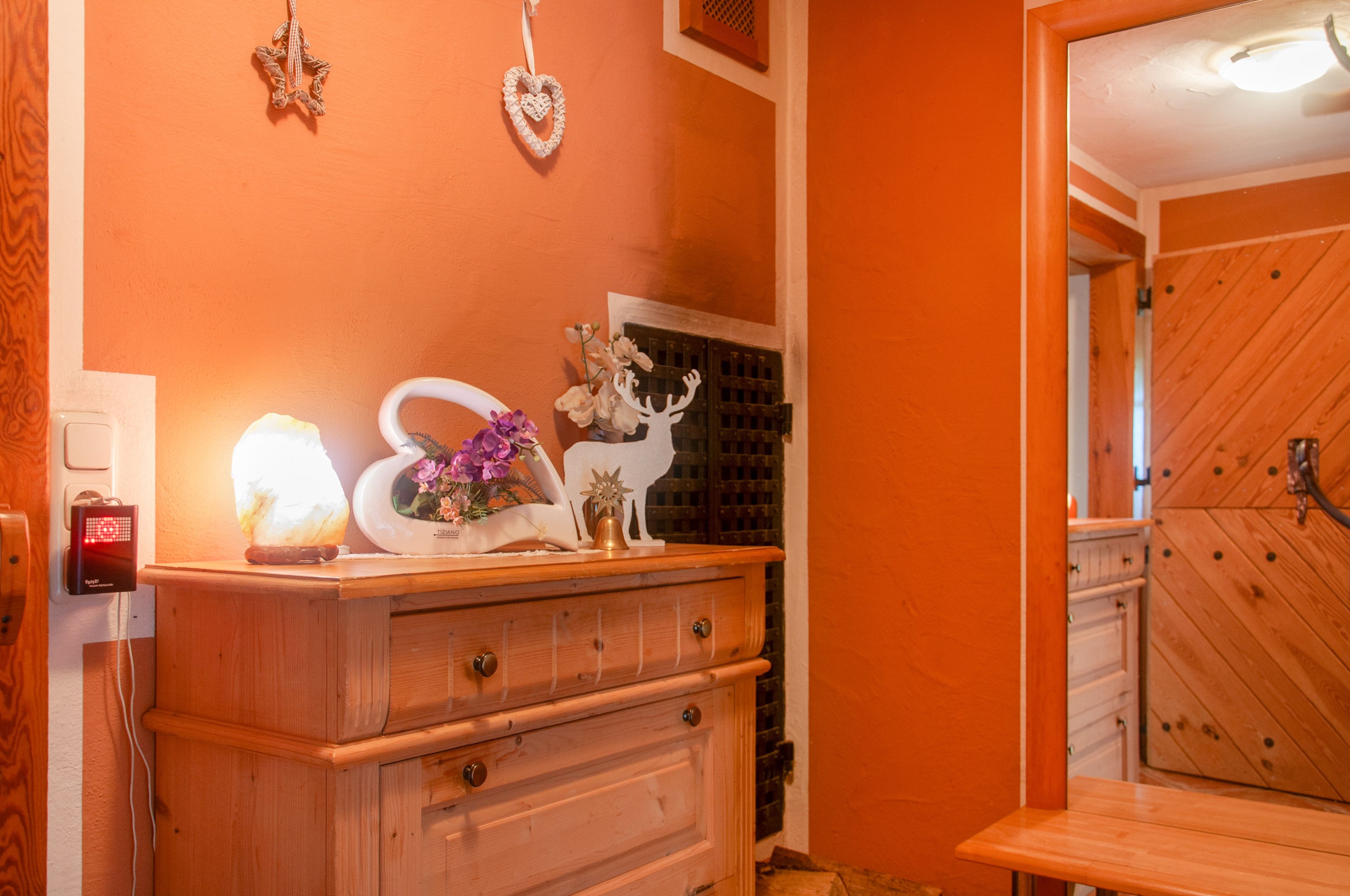 A wooden dresser with drawers, a white vase with purple flowers, and a white star-shaped ornament on the wall.