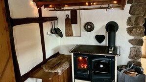 A stone wall, a fireplace with a black stove, and a hanging pot rack.