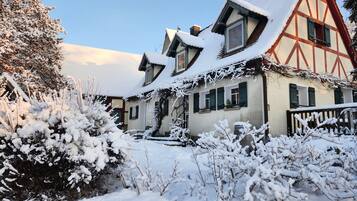 A traditional chalet with a steep roof, wooden beams, and a snow-covered garden.