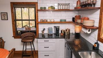 Una cocina con armarios blancos, encimera de madera, cafetera y diferentes utensilios de cocina.