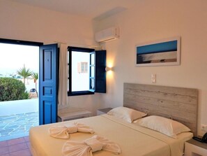 Una habitación de hotel con cama, mesita de noche, equipo de aire acondicionado y vista al exterior.