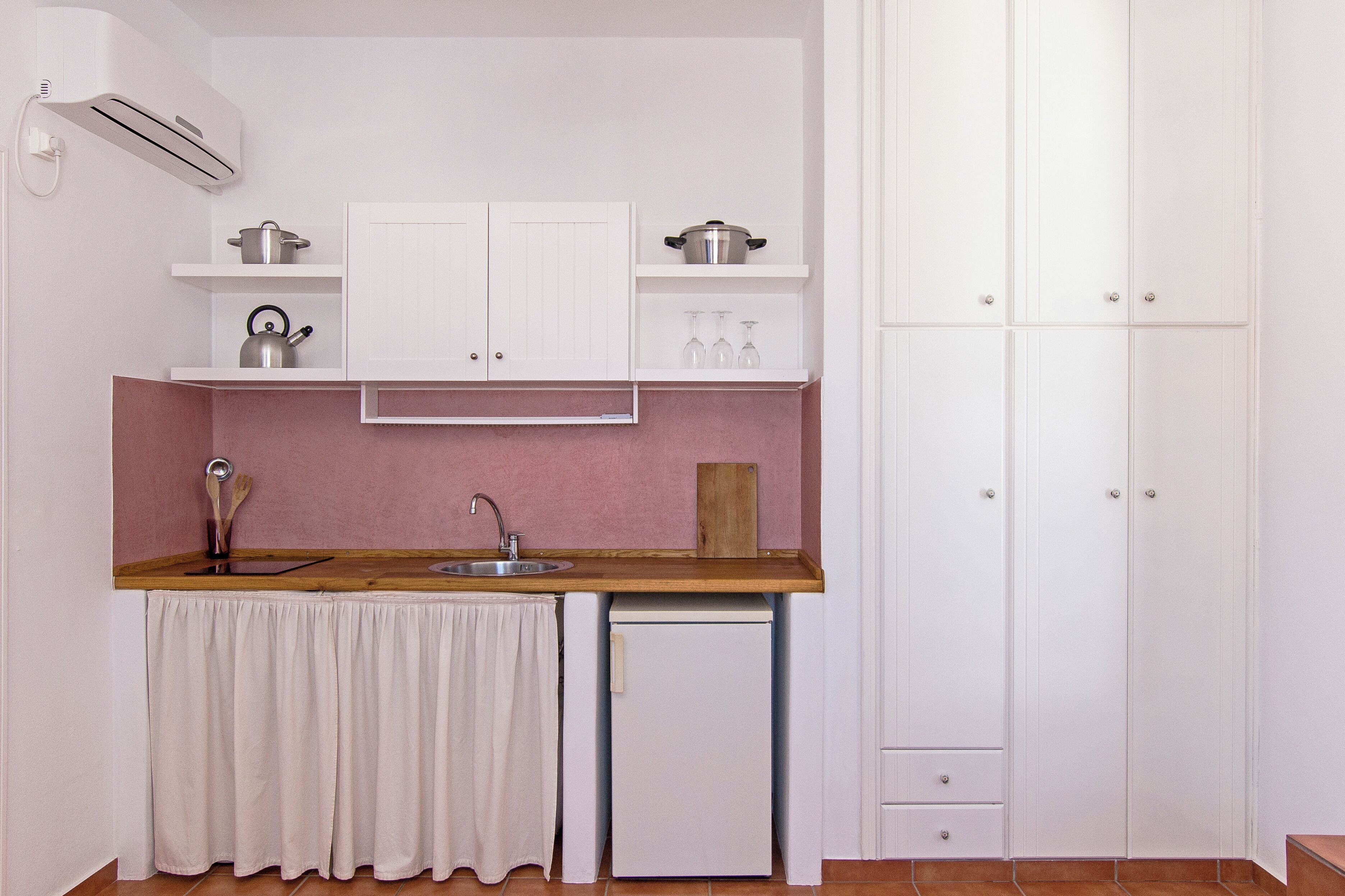 A compact kitchen with white cabinets, a wooden countertop, a sink, and a small refrigerator.